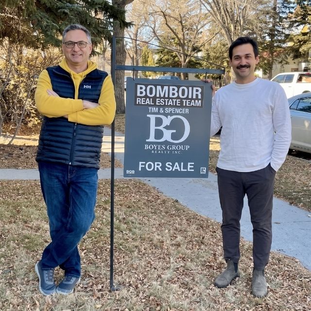 Tim and Spencer Bomboir standing beside their Bomboir Real Estate Team for-sale sign on a Saskatoon street
